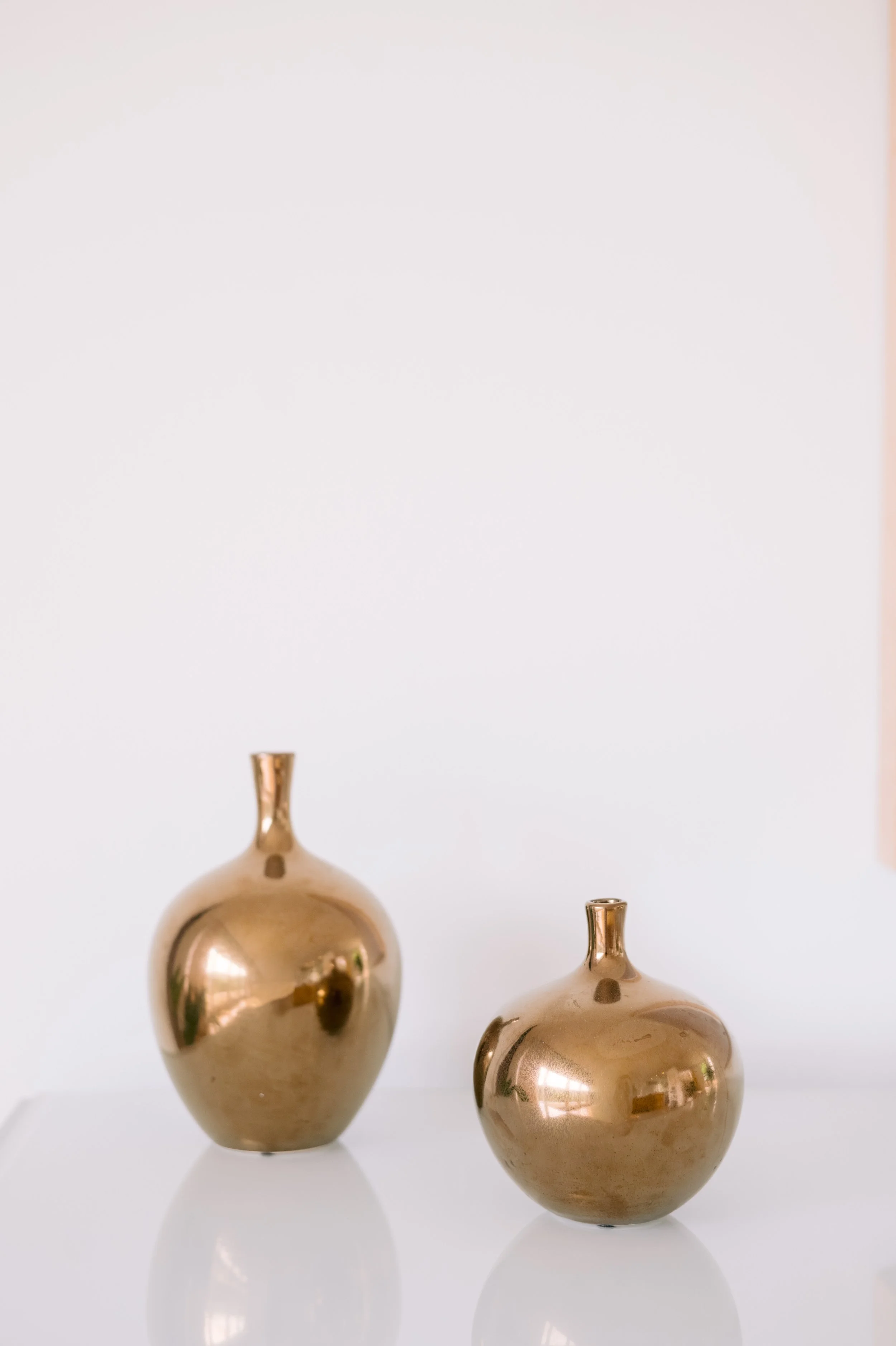 Two gold vases of different sizes against a white backdrop