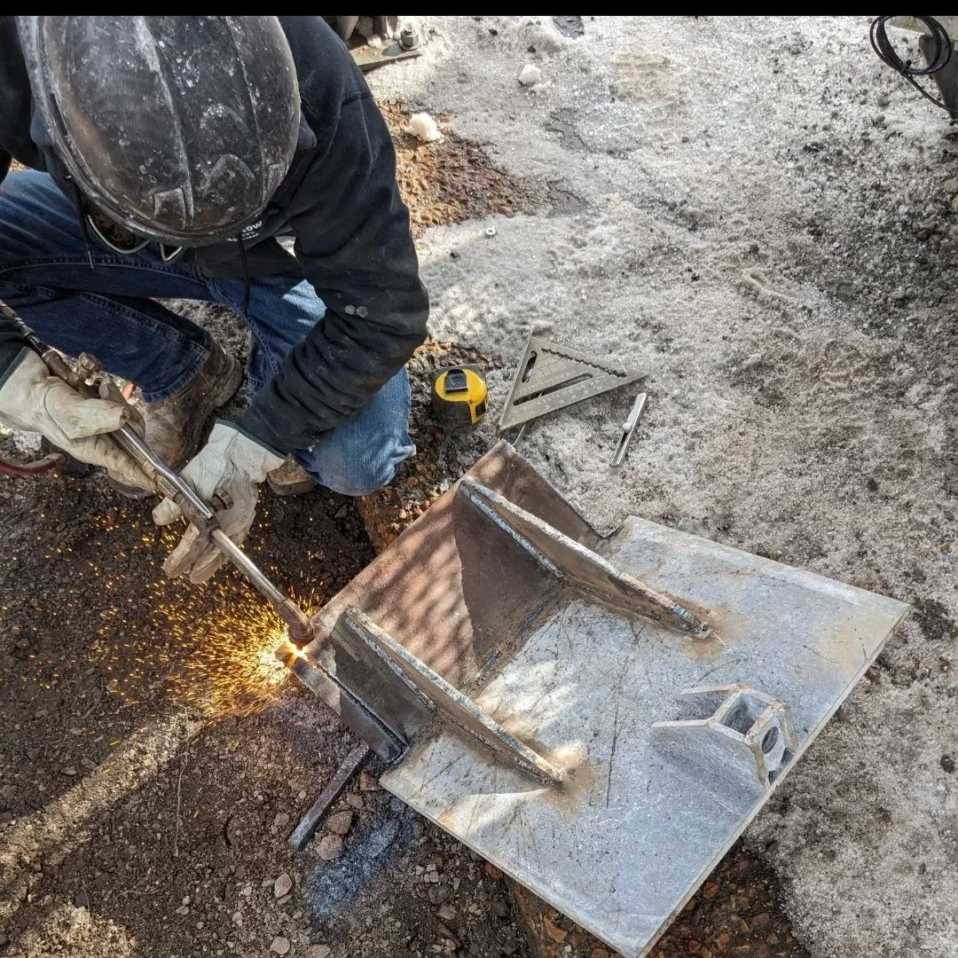 A worker wearing safety gear welding a metal structure, with sparks flying, on a construction site.