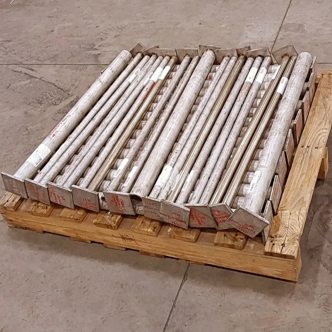 A box with metal pipes resting on a wooden pallet in a workshop with tools and equipment in the background.