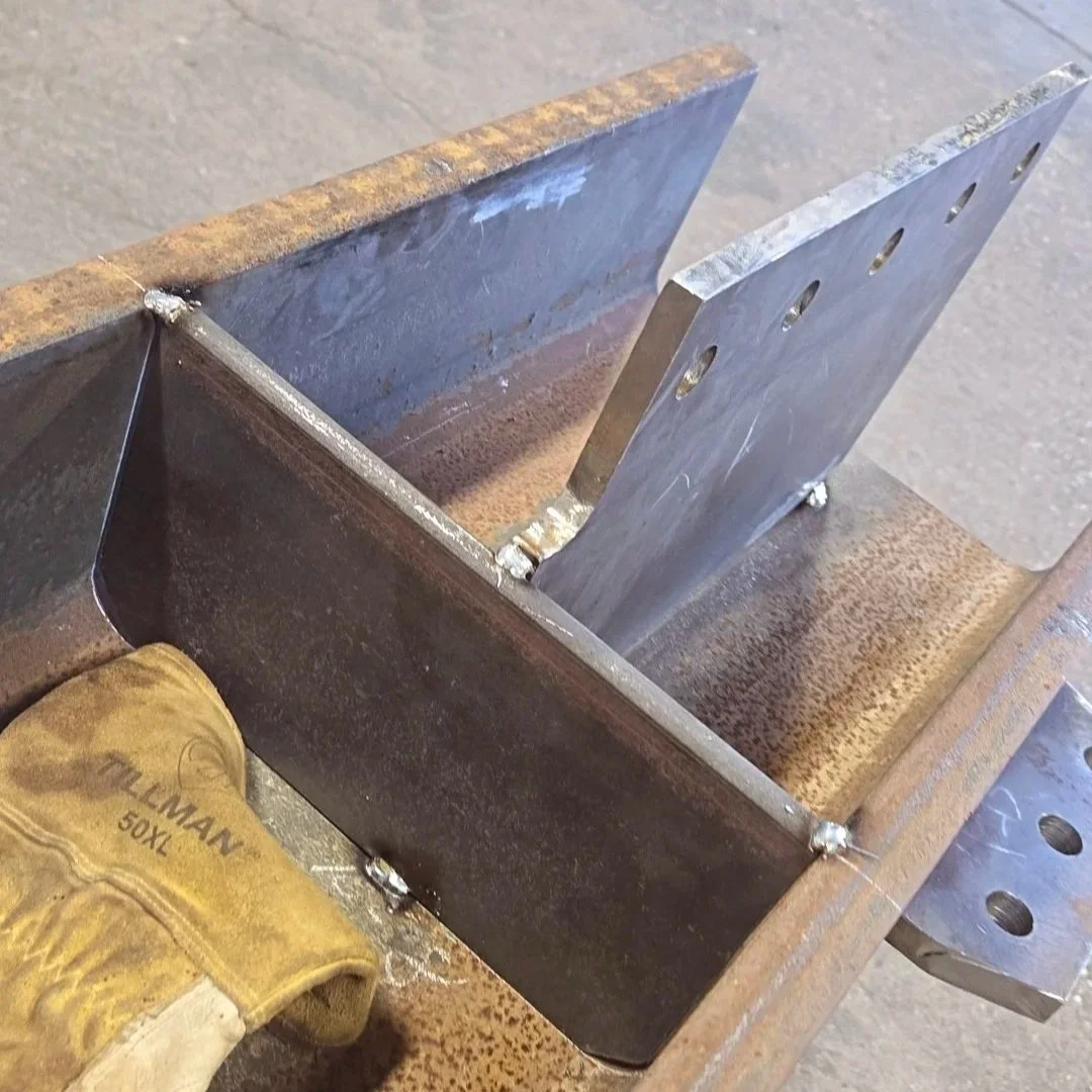 Close-up of a metal welding project with a weld glove resting on a rusty metal workbench.