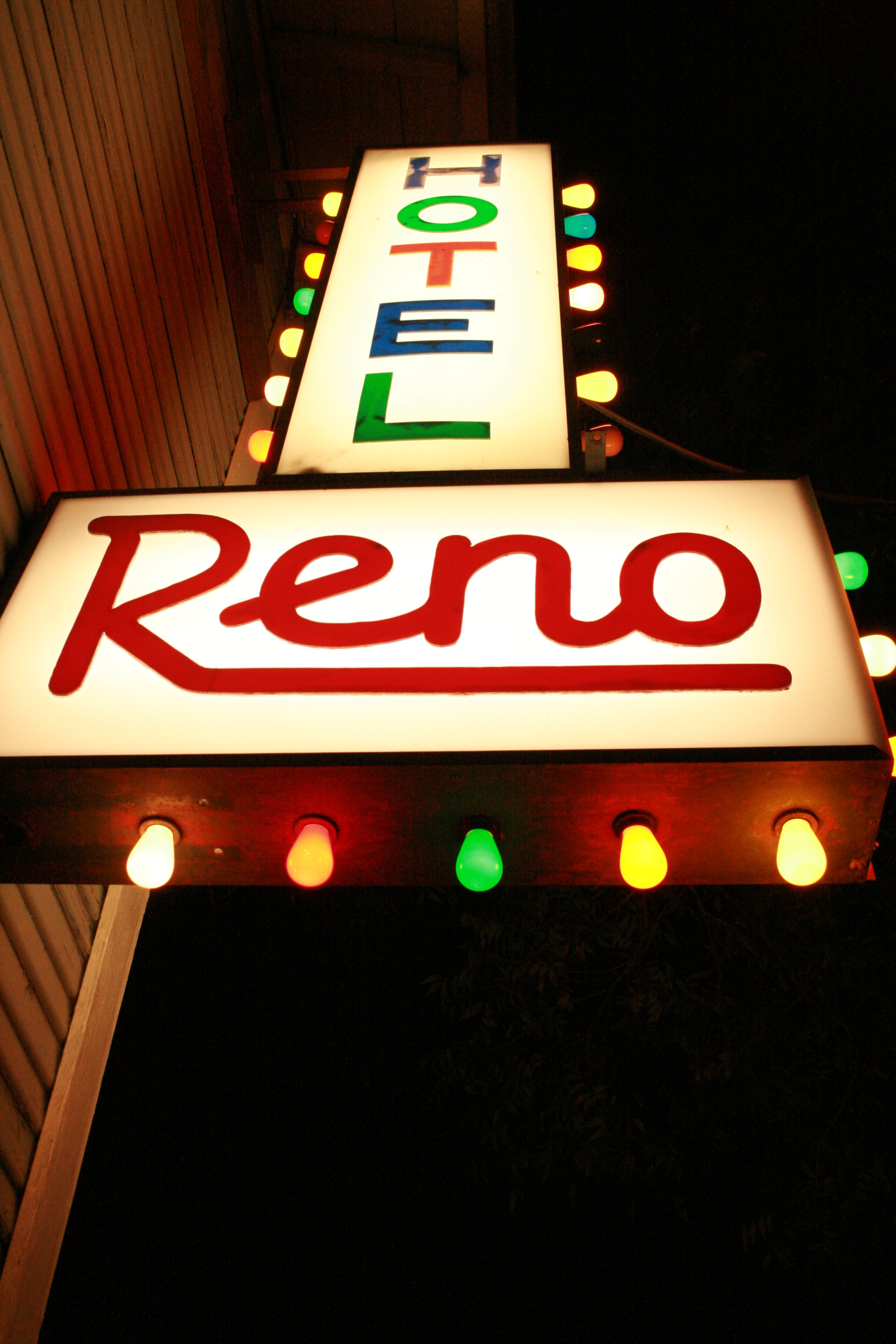 Illuminated sign with the word "Reno" in red and the word "HOTEL" in multicolored letters, surrounded by multicolored light bulbs, at night.