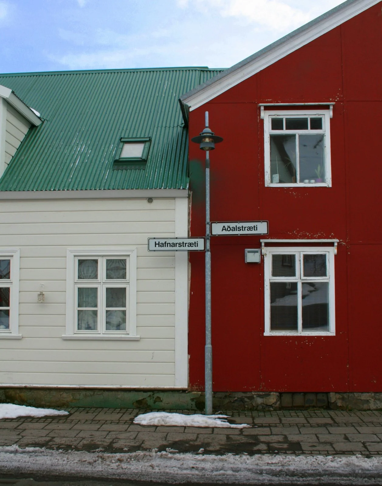Street corner with signs for Hafnarstræti and Aðalstræti, buildings with white and red walls, green metal roof, and snow on the sidewalk.