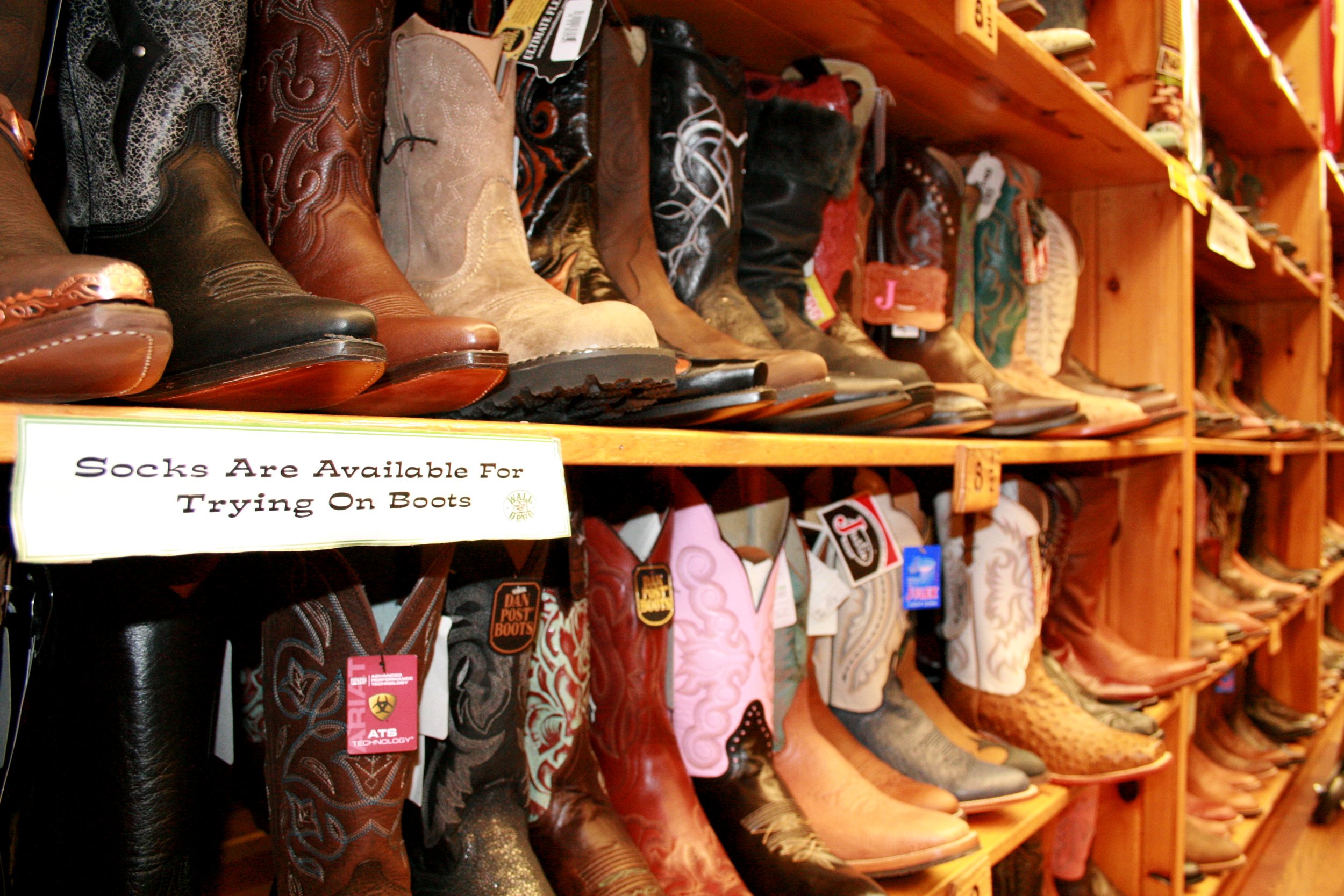 Shelves of cowboy boots in a store with a sign that reads, 'Socks Are Available For Trying On Boots'.