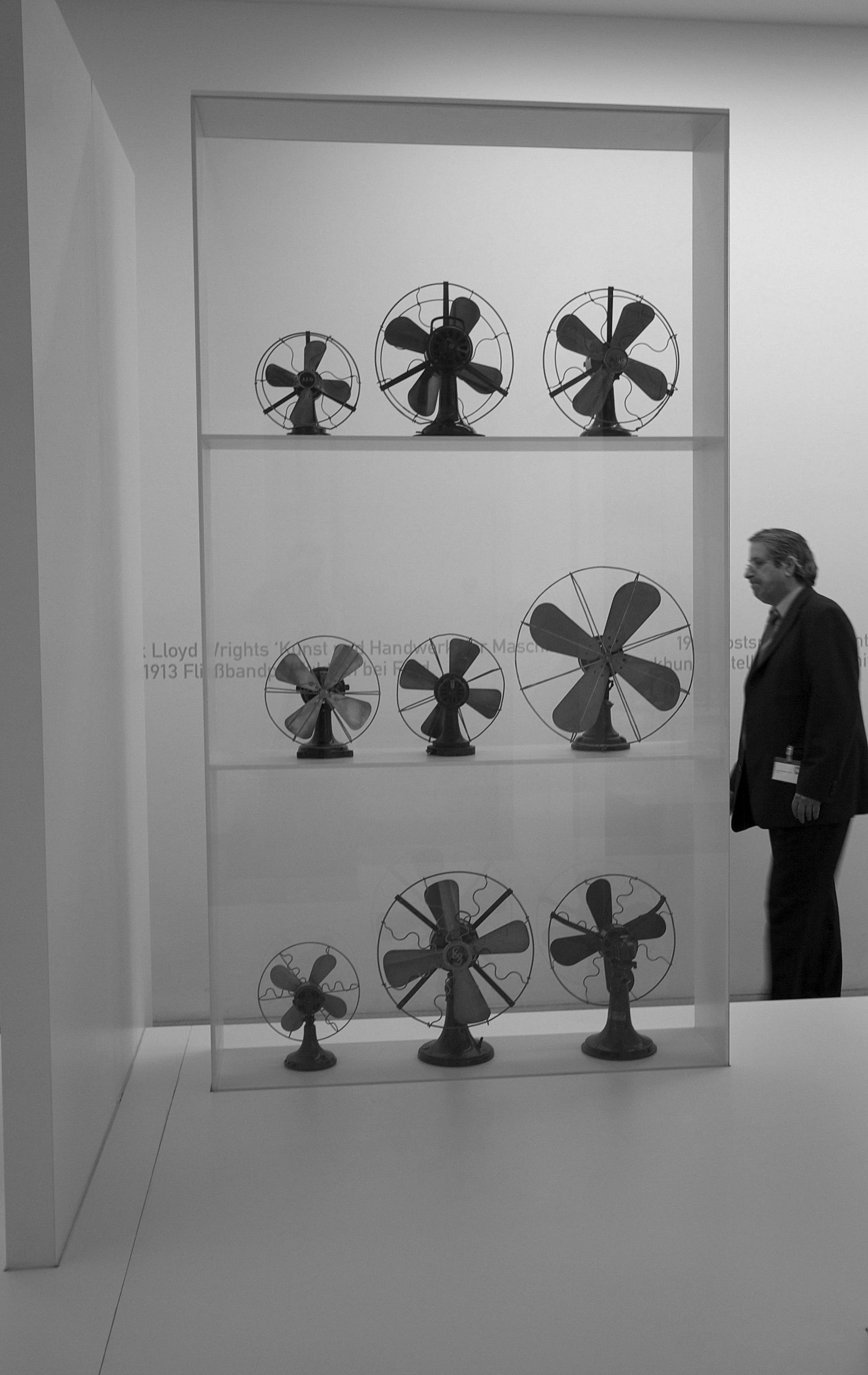 Display of antique electric fans arranged on shelves in a museum, with a person observing the exhibit.