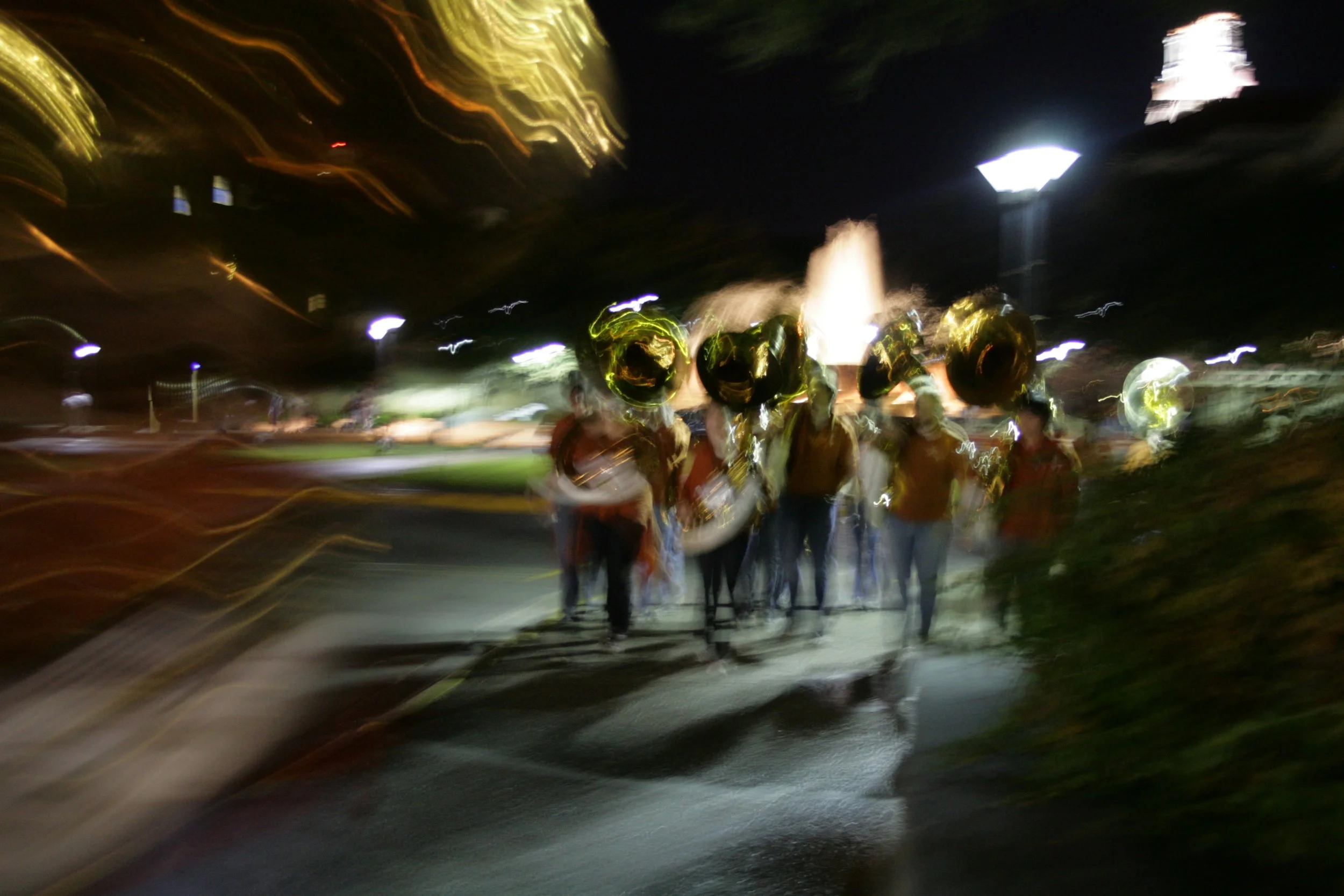 A group of people walking at night, holding shiny gold balloons. The photo is blurry and has streaks of light, indicating motion and a long exposure.