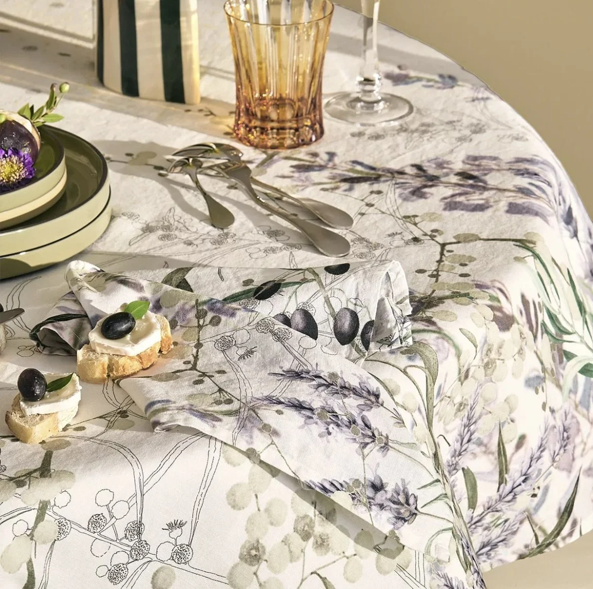 A table set with a luxury floral tablecloth, a layered bowl, a tall orange glass, and silverware rented from Akita Event Rentals for weddings, galas, and other events in Omaha, NE.