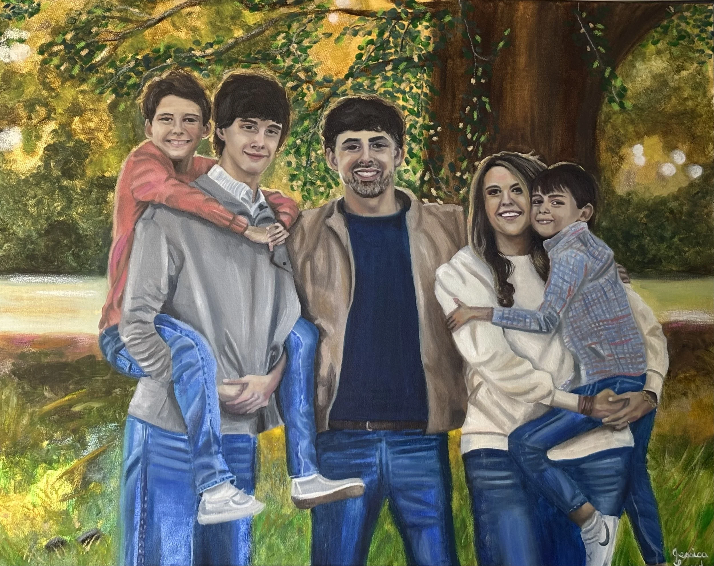 Afamily of six posing outdoors in front of a large tree with yellow and green leaves. The father and mother are in the center, with three children; two boys and a girl, and another boy being carried on the father’s back. They are all smiling and dressed casually.