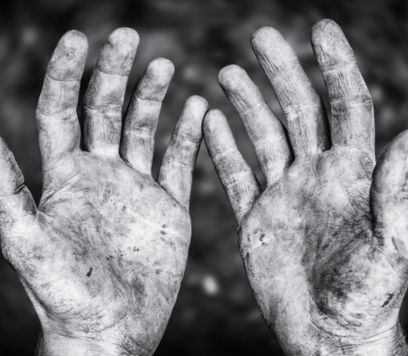 Two dirt-covered hands held up with palms facing the camera, in black and white.