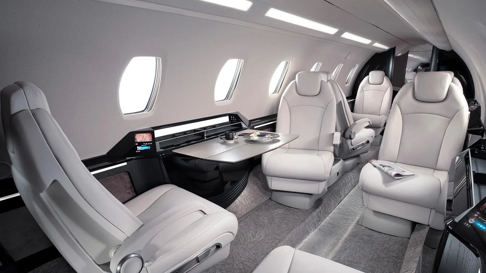 Interior of a luxurious private jet with white leather seats, windows, and a small table with food and drink.