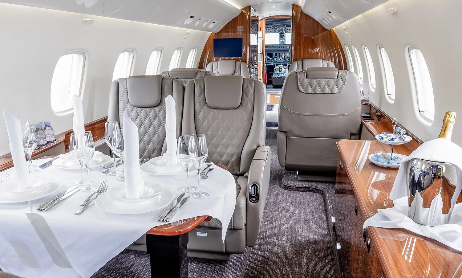 luxury jet interior with a dinner table, elegant settings, champagne, and plush leather seats.