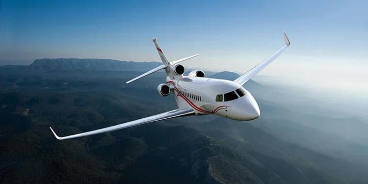 A white private jet flying in clear blue sky over mountains.