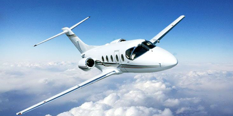 A white private jet flying in the sky above clouds.