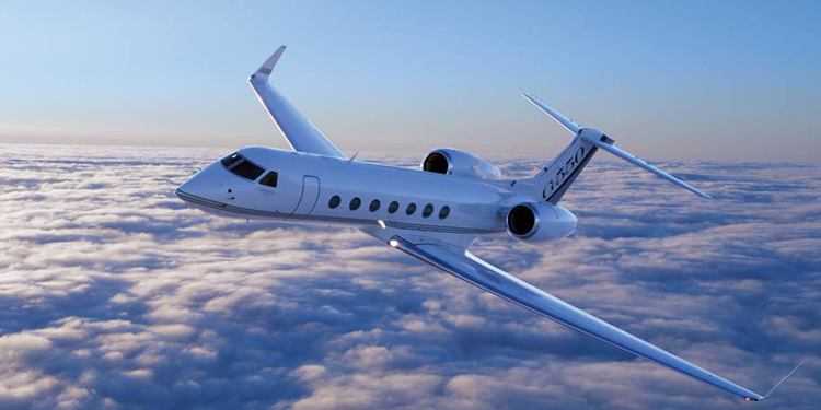 A white private jet flying above the clouds with a clear blue sky in the background.
