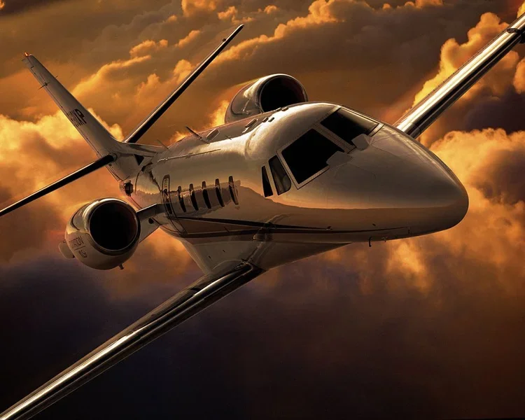 A sleek private jet flying through a dramatic sunset sky with orange and gold clouds.