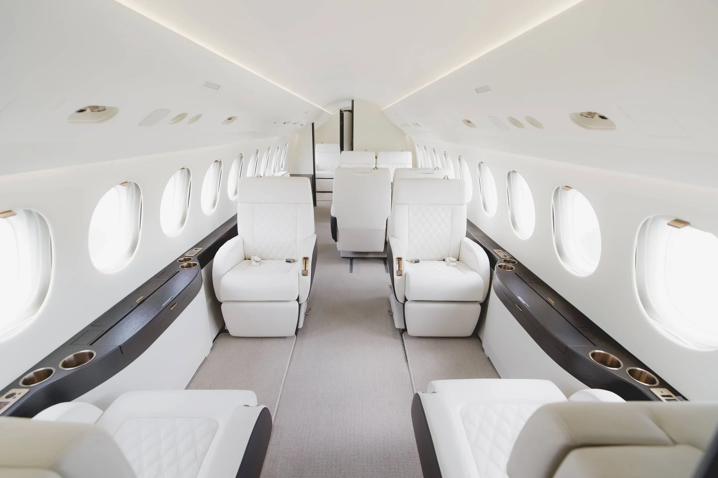 Interior of a private jet with white leather seats and multiple windows.