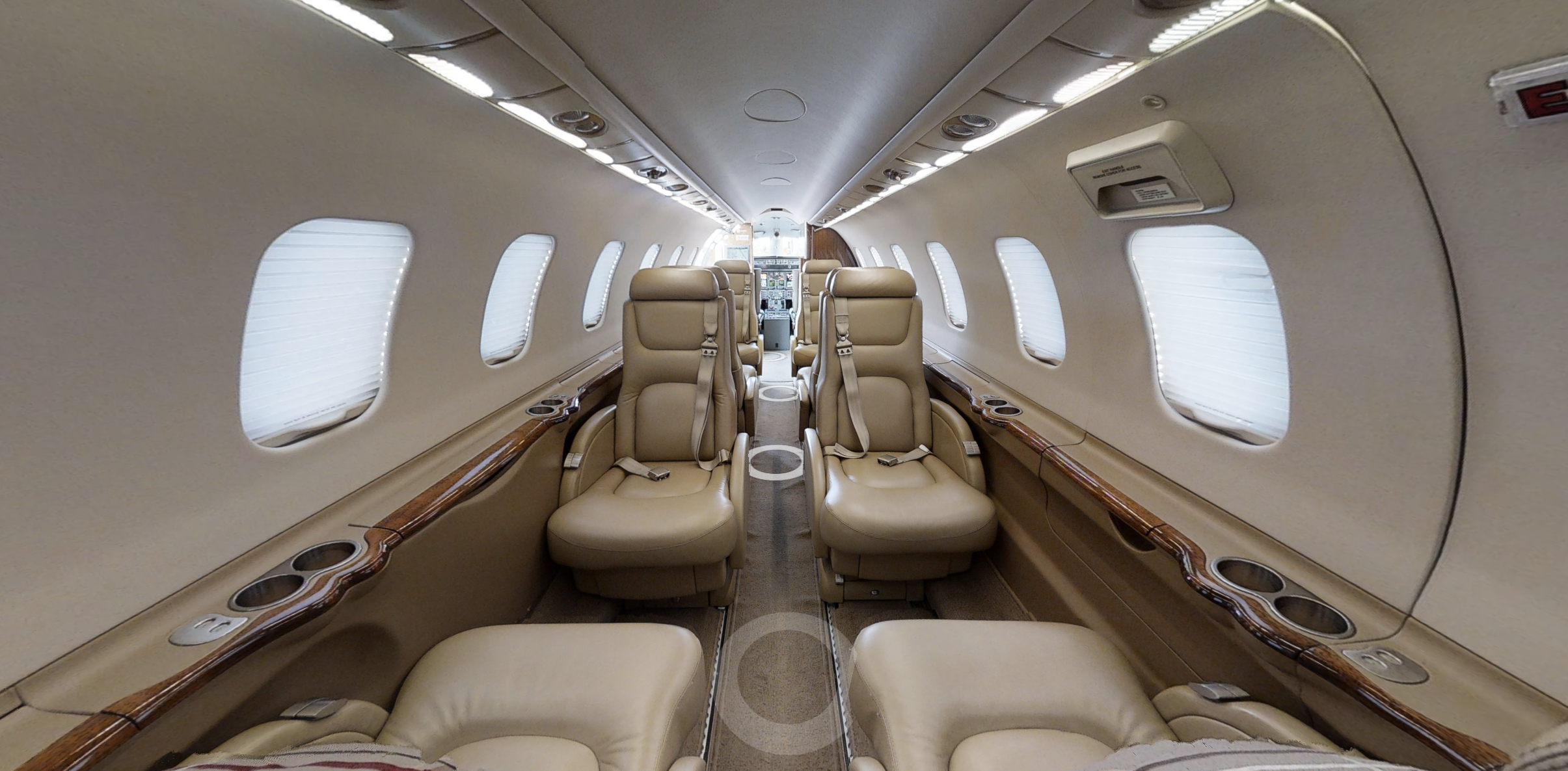 Interior of a private jet with beige leather seats, windows with closed blinds, and wood accents along the sides.