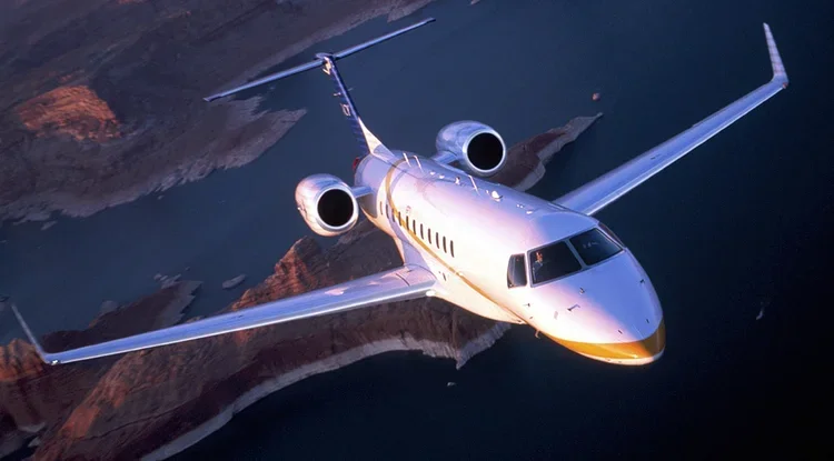 A private jet flying over a body of water with land in the background.