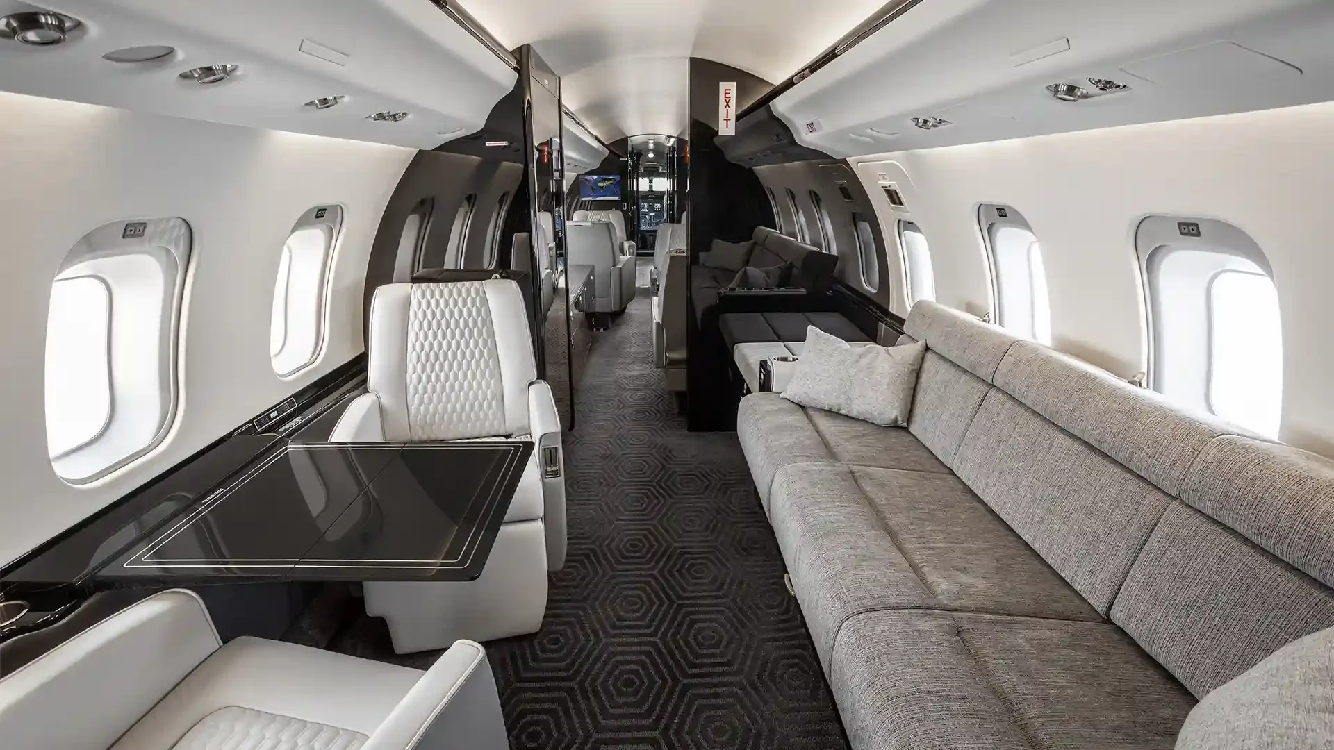 Interior of a luxury private jet with beige and white seating, a black table, and multiple windows.