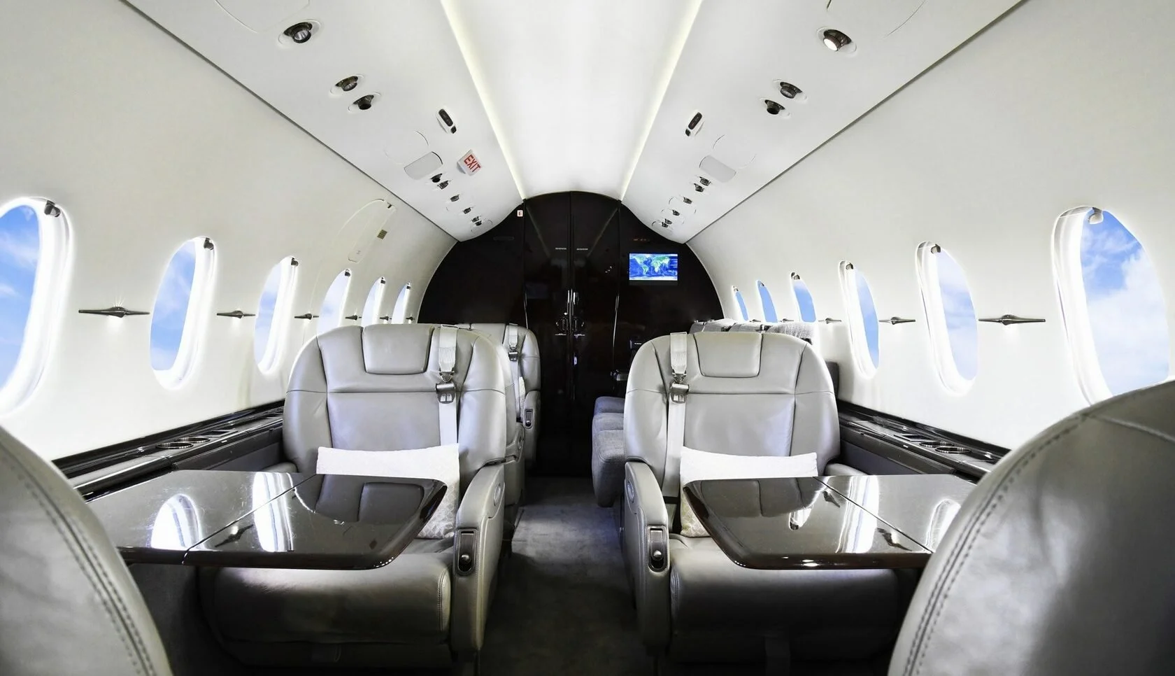 Inside view of a private jet cabin with leather seats, small tables, and windows showing sky and clouds.