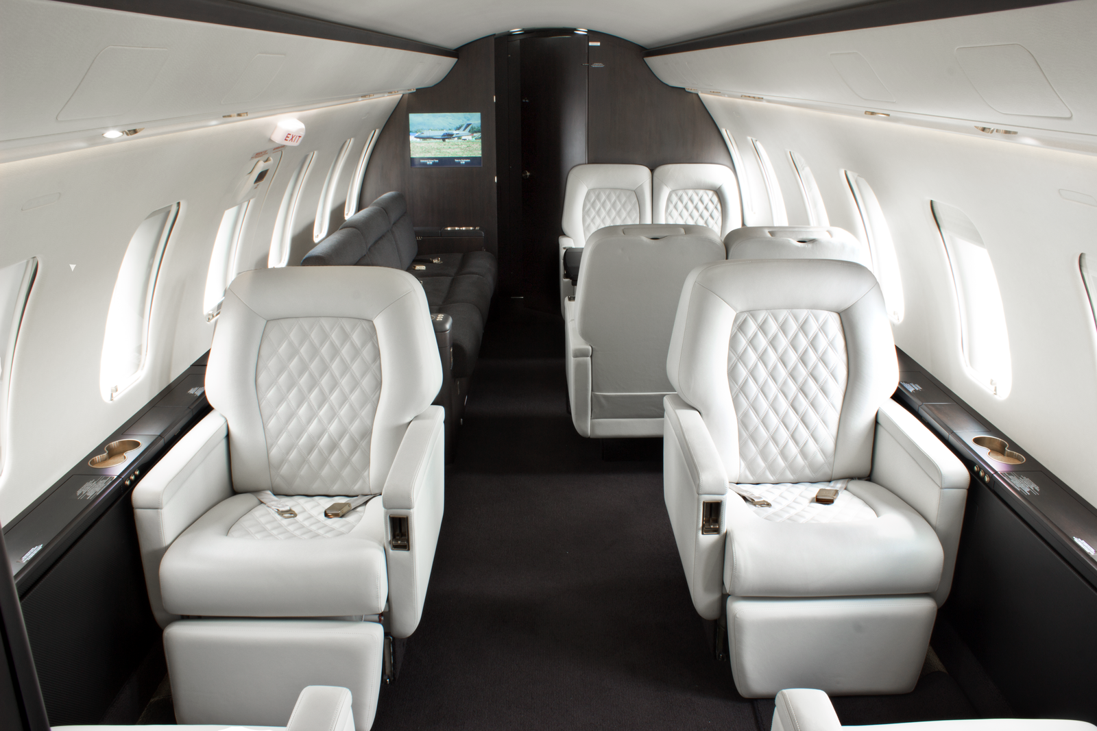 Interior of a private jet with white leather seats, windows, and a small TV screen on the wall.