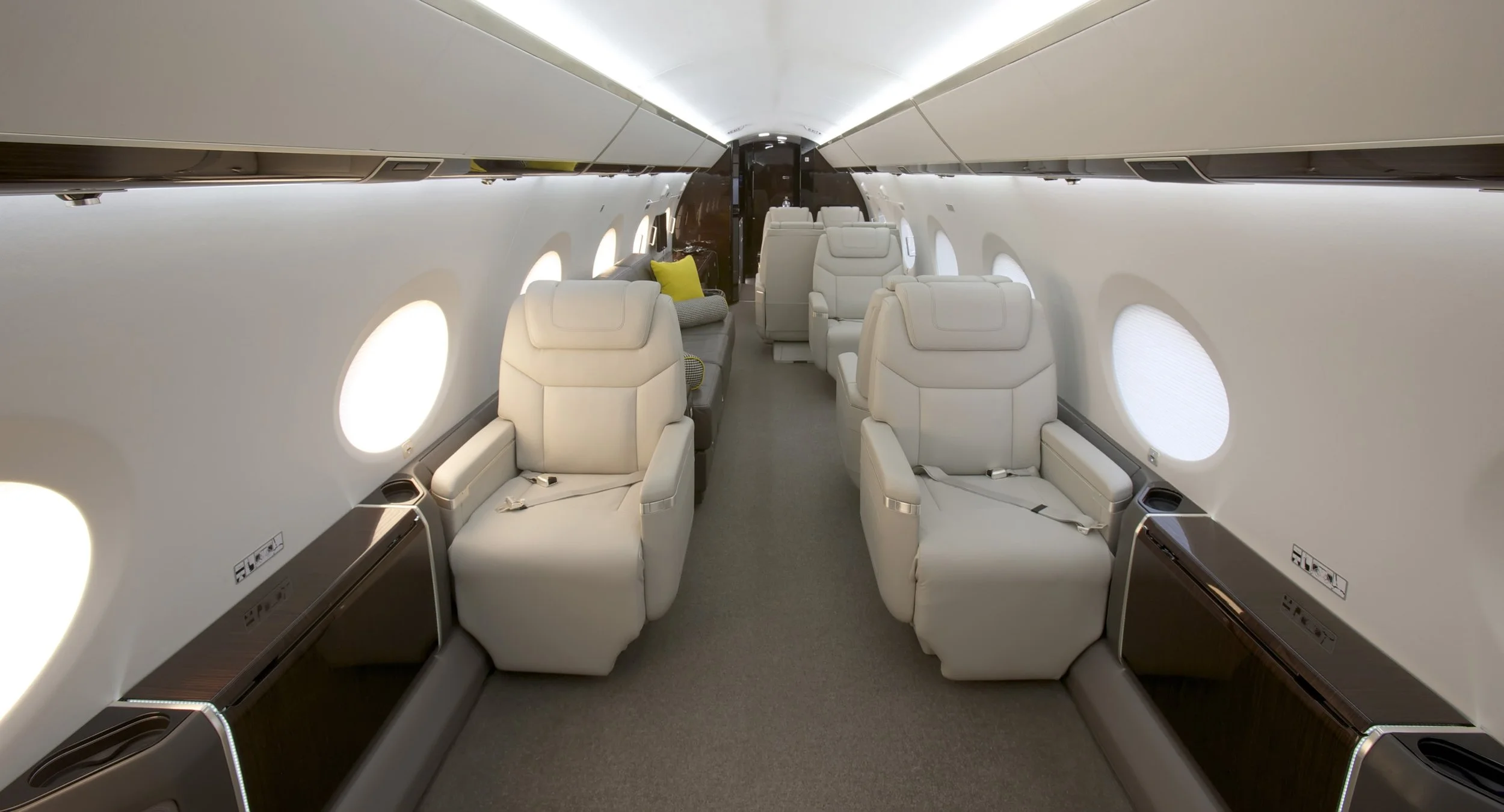 Interior of a private jet with white leather seats, small pillows, and windows along the walls.