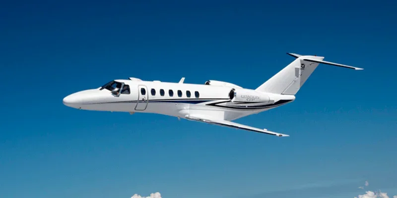 A white private jet flying in a clear blue sky.