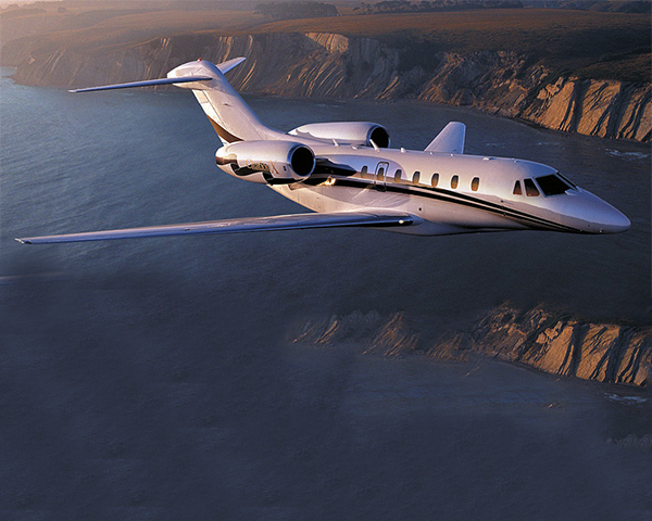 A luxury private jet flying over mountains during sunset.
