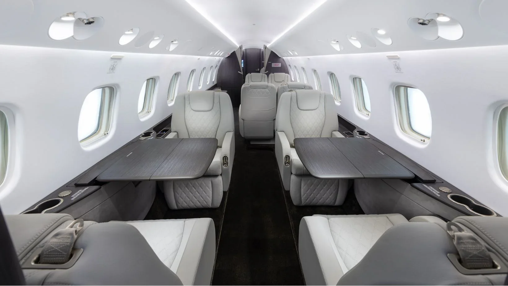 Interior of a private jet with white leather seats, foldable tables, and windows along both sides.