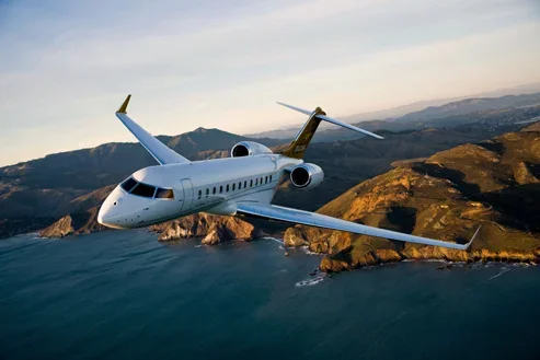 A private jet flying over a coastal landscape with hills and water.