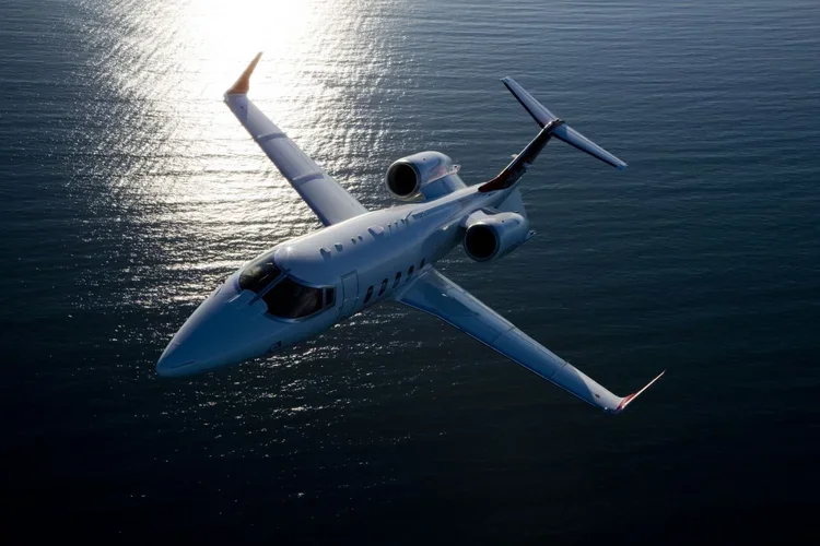 A private jet flying over a body of water during sunset.
