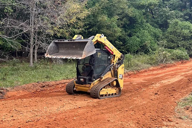 Compact track loader shaping a new dirt road through the woods