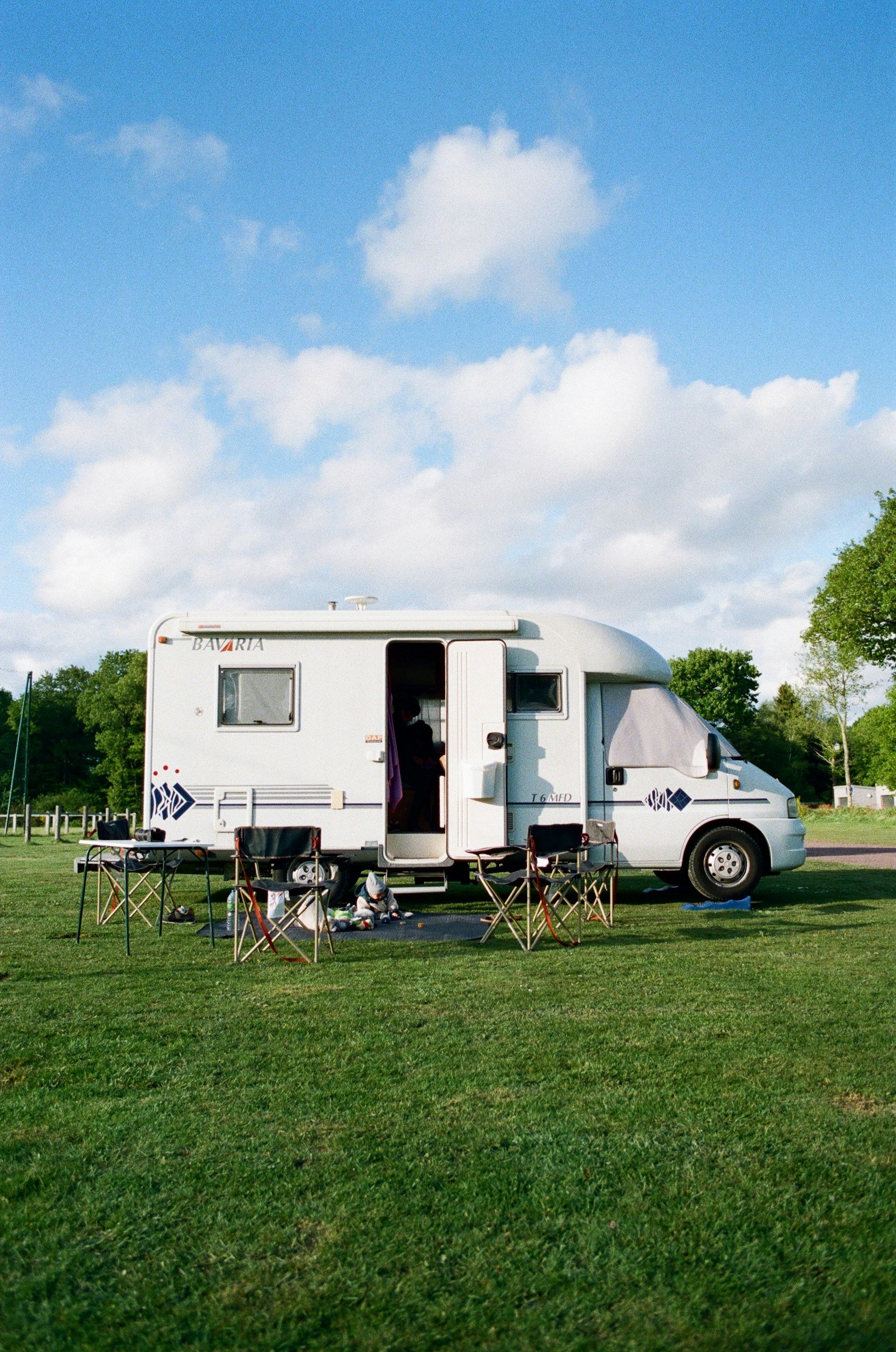 En vit husbil parkerad på en gräsmatta med campingstolar och barnleksaker framför.