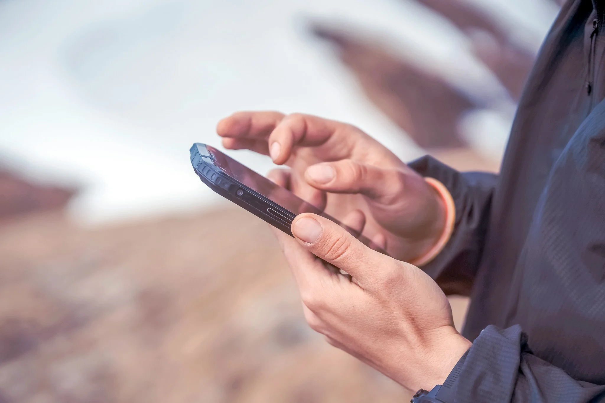 Person som använder en smartphone utomhus, nära vatten och natur.
