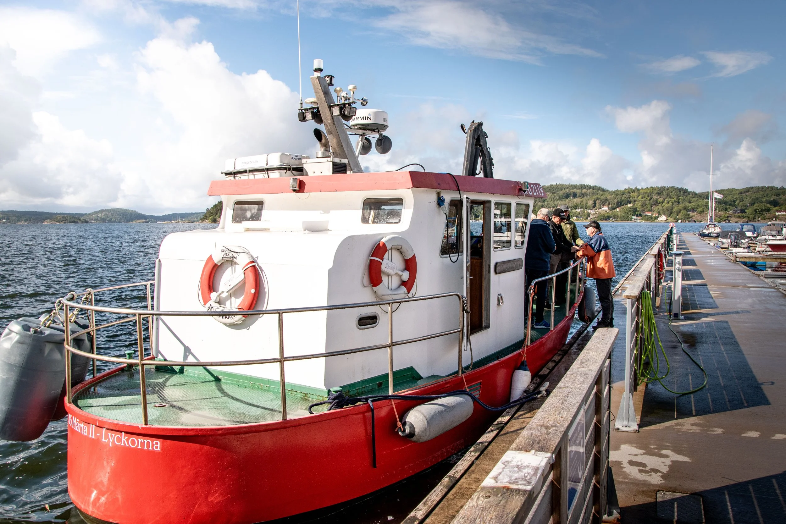 En röd fiskebåt längst ut på en kaj, med några personer som står och samtalar på däcket.