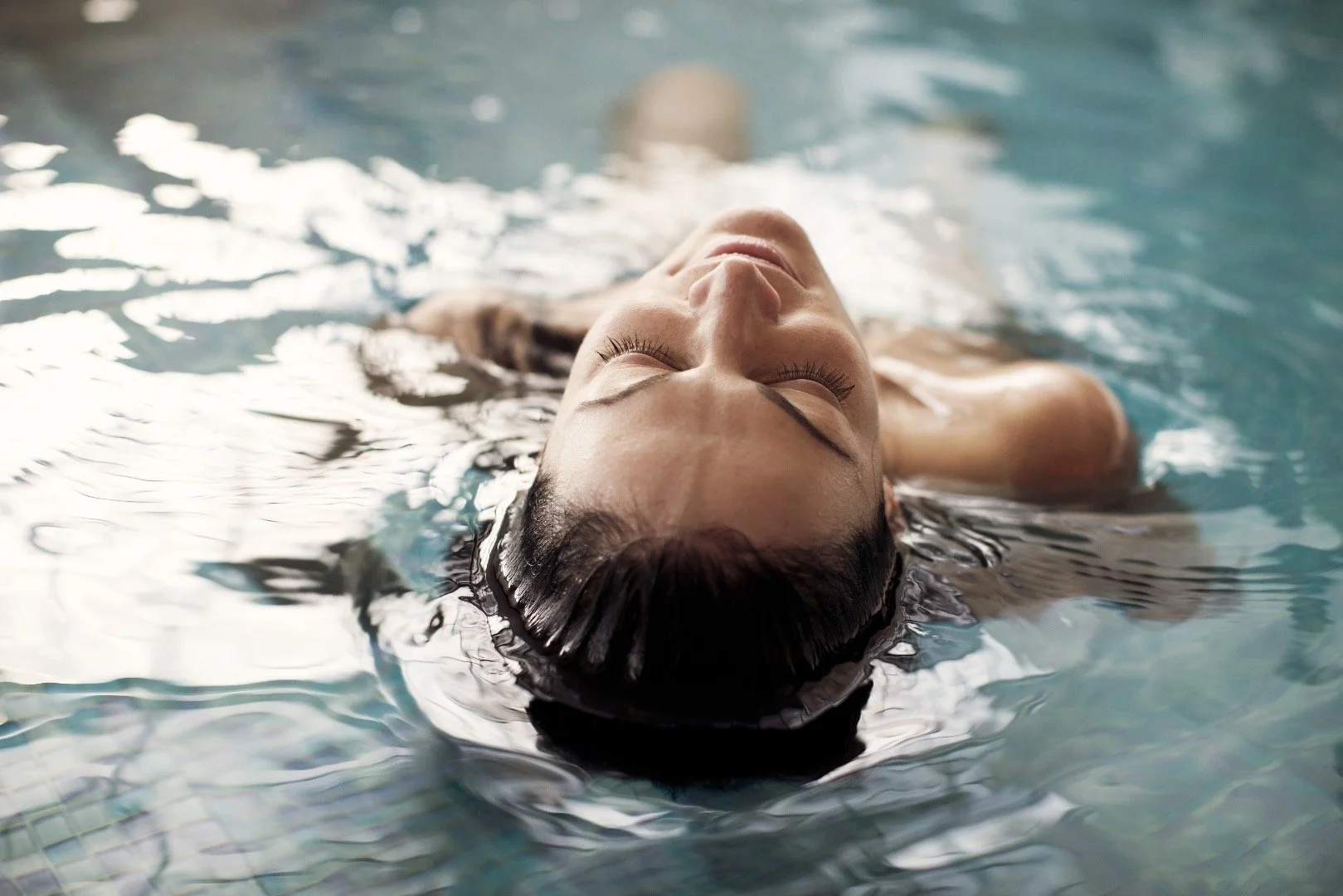En woman flyter på rygg i en simbassäng med ögonen stängda, slappnar av.
