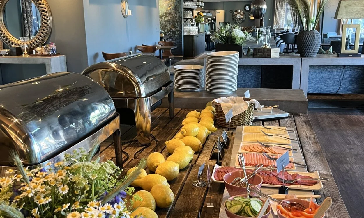 Buffébord med lemonader, skivade grönsaker, kallskuret, ostar och varma rätter i en restaurangmiljö.