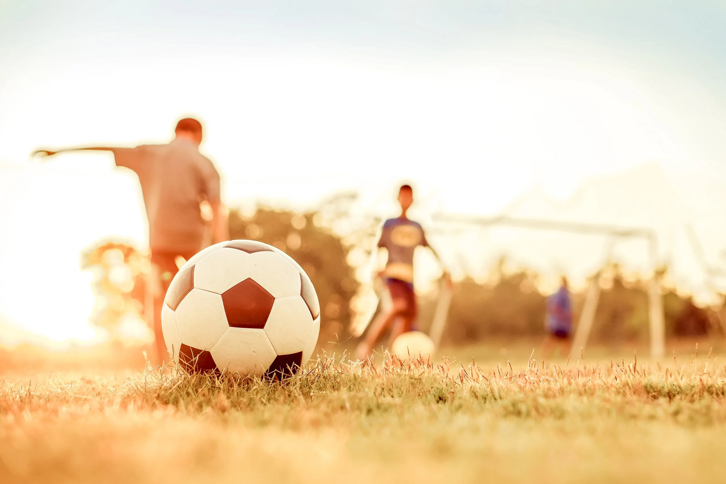 Fotografi av barn som leker med fotboll på en fotbollsplan under solnedgången.