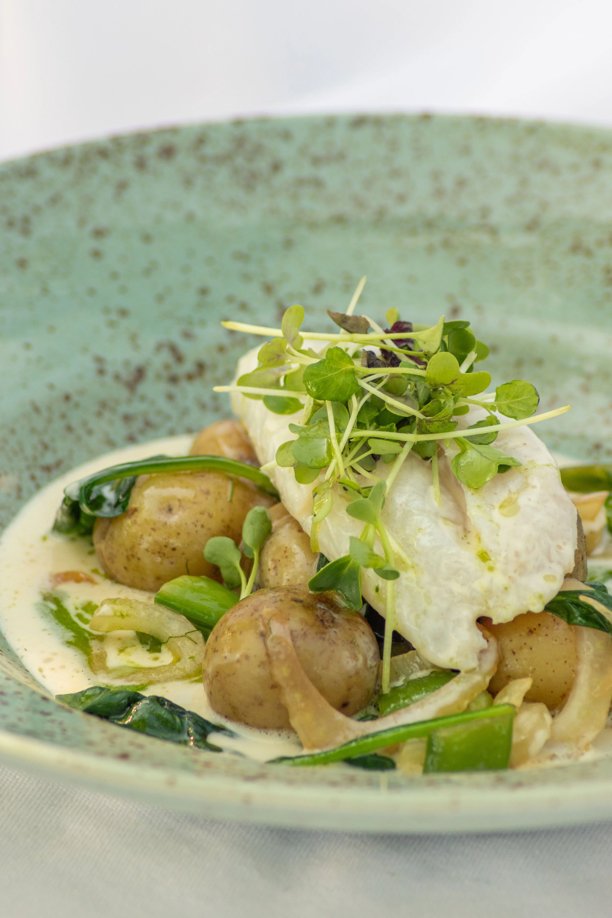 En tallrik med potatis, grönsaker, torsk och microgreens i en grön keramikskål.