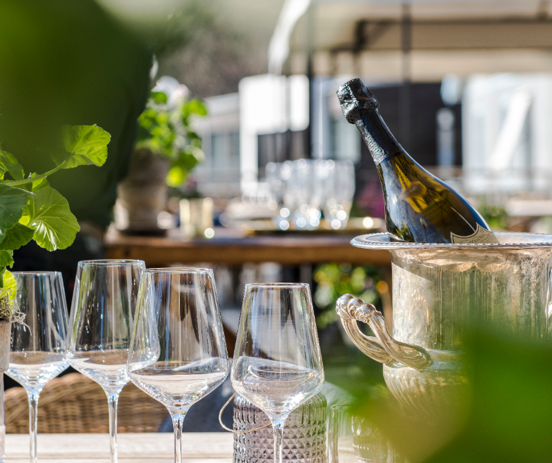 Kubik av is med en vin- eller champagneflaska och tomma glas på ett utomhusbord.