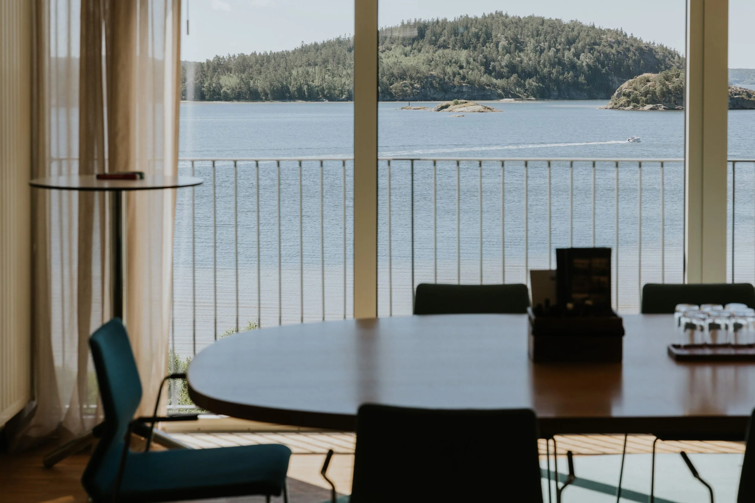 Intérieur d'une salle de réunion avec vue sur la mer et les îles depuis de grandes fenêtres. La pièce comprend une table ronde, quelques chaises et une petite table d'appoint.