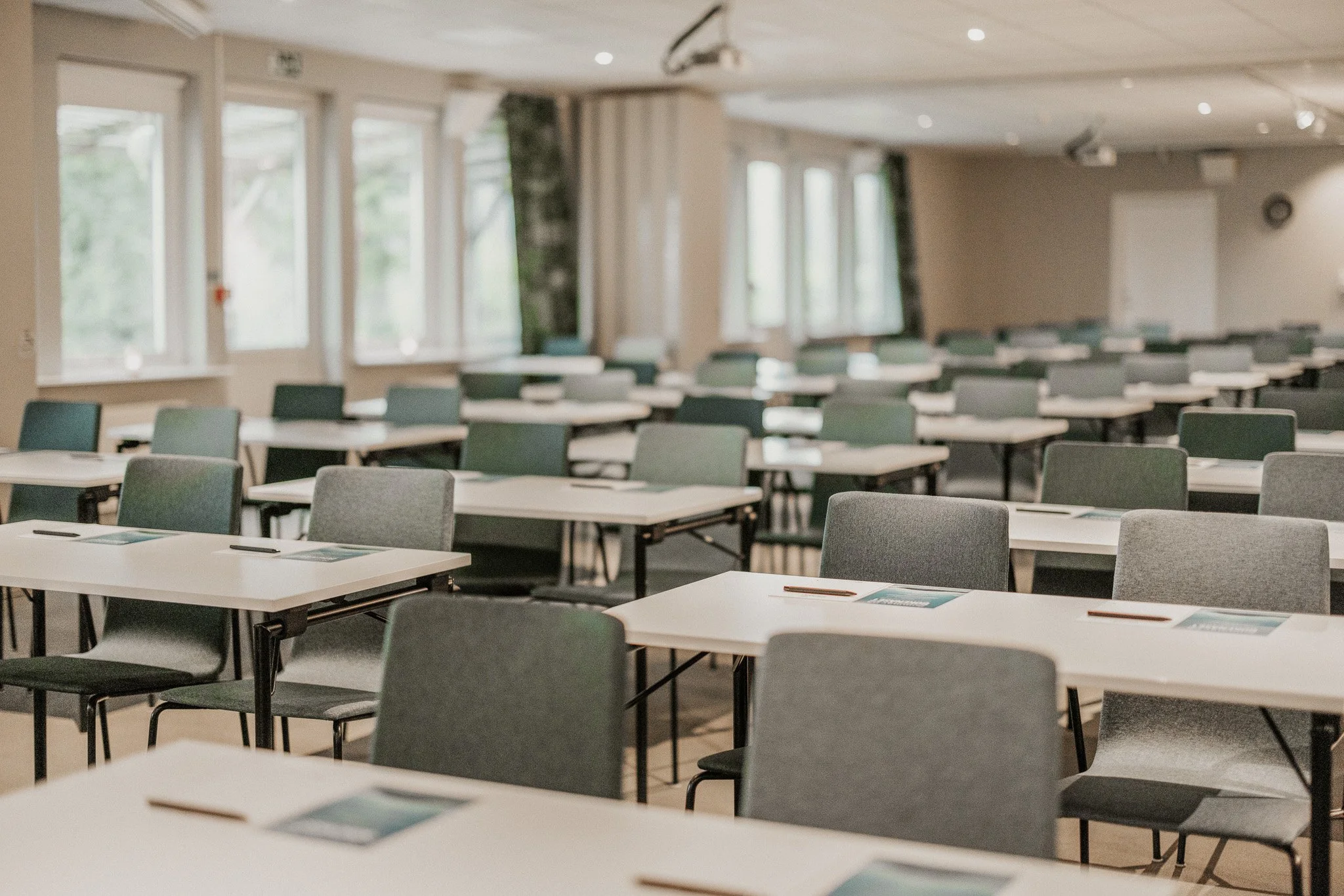Une salle de conférence vide avec plusieurs rangées de chaises et de bureaux, de grandes fenêtres et une atmosphère calme.