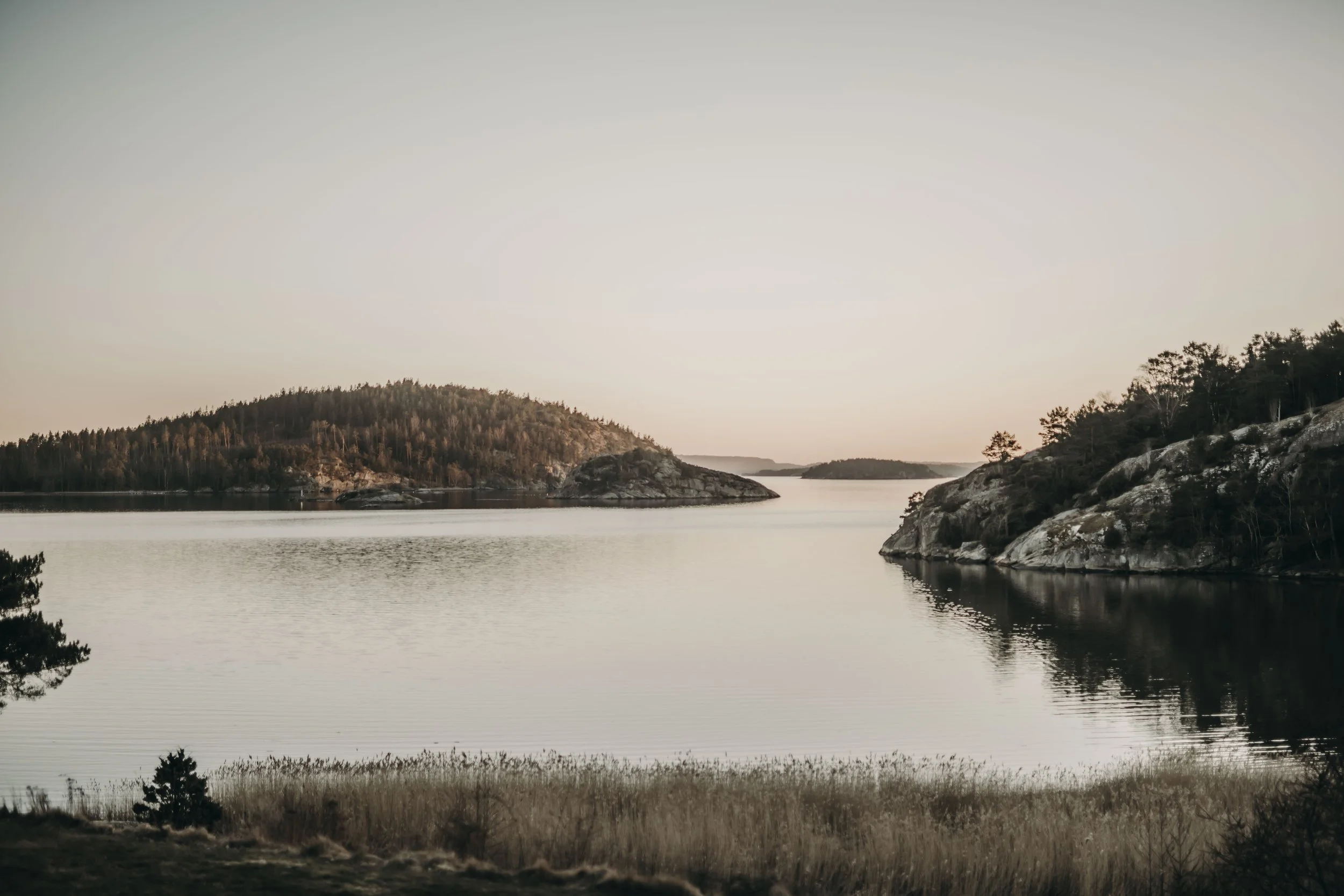 Un fjord paisible entouré de falaises boisées et d'îles au coucher ou au lever du soleil.