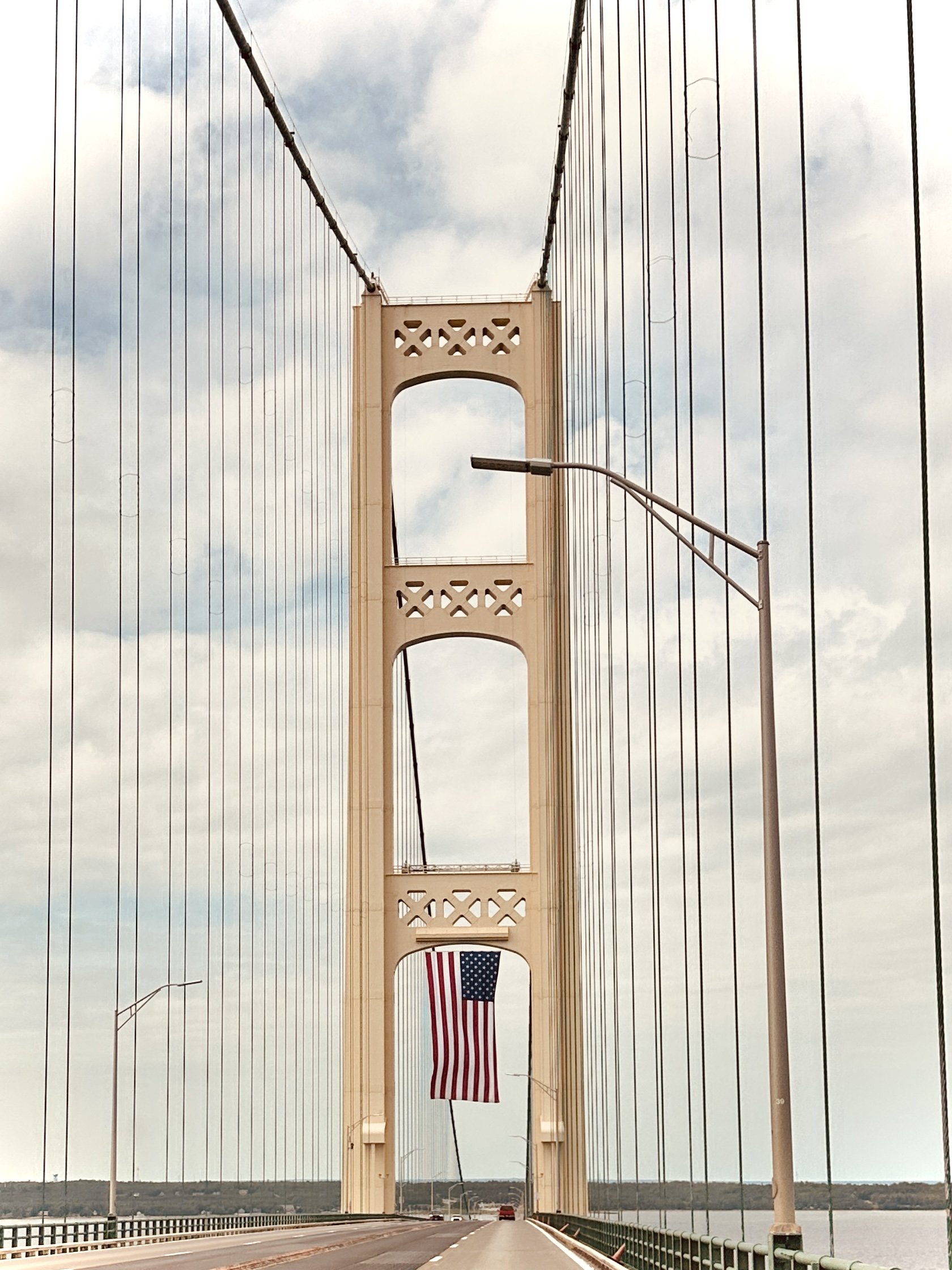View of the Mackinac bridge in Michigan with an American flag hanging from the middle of the bridge and lamp posts along the road.