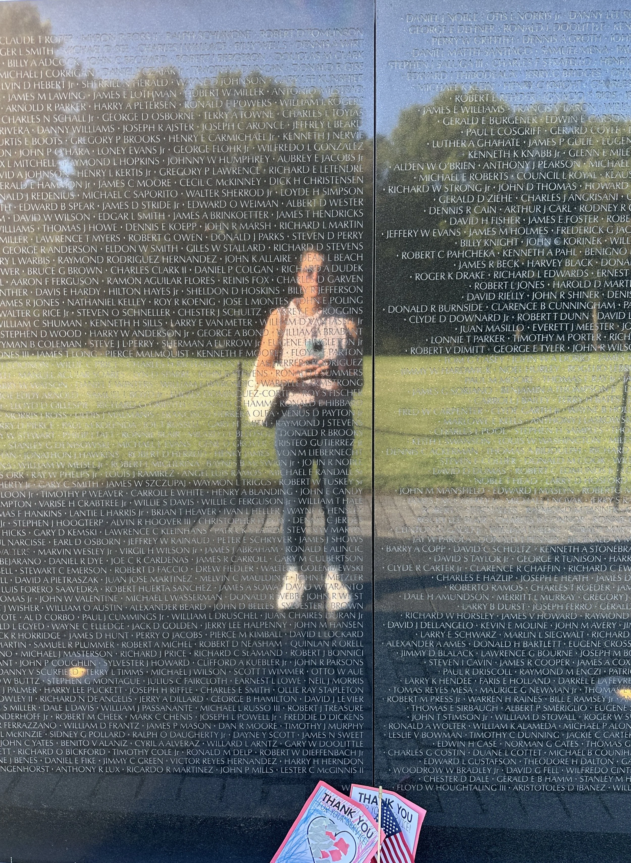 Vietnam Memorial wall engraved with numerous names of veterans, with a person in the center. A small thank you card is placed at the bottom, featuring an American flag and 'Thank You' message.