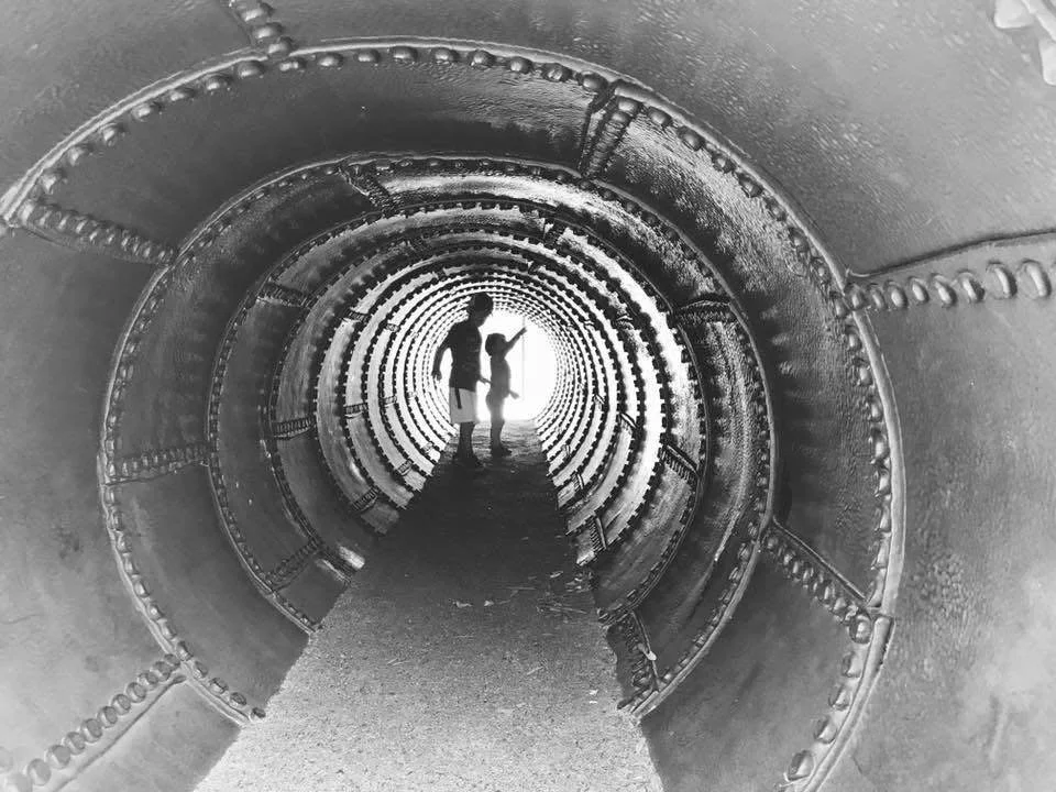 Silhouettes of a man and woman holding hands inside a cylindrical, tunnel-like structure.