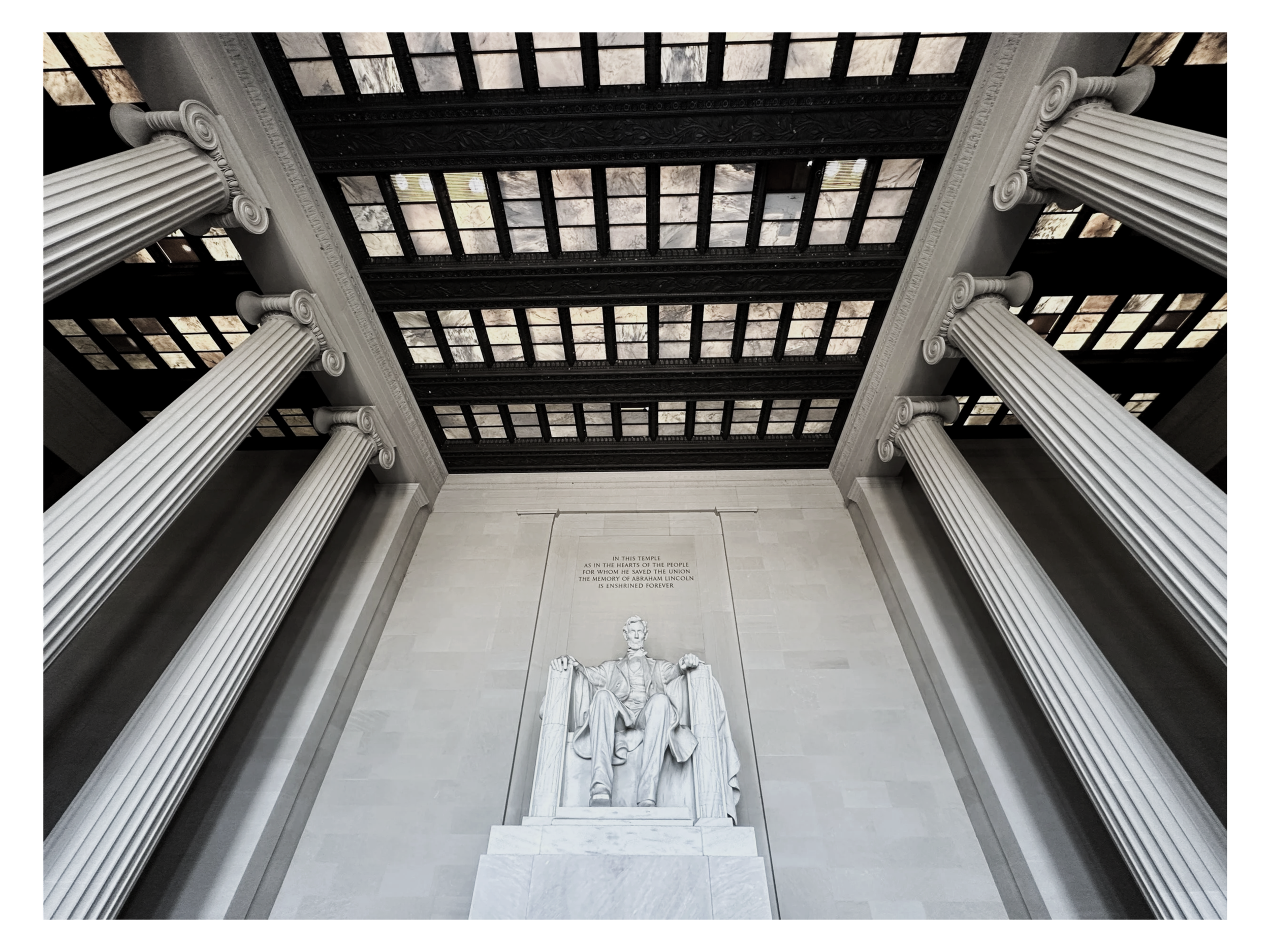 Looking up at the Lincoln Memorial statue with tall, fluted columns and a carved inscription on the wall behind it in the memorial's interior.