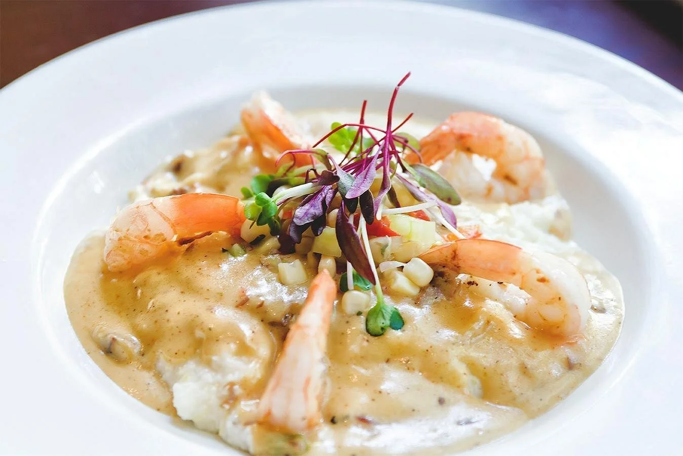 A white bowl filled with seafood chowder topped with shrimp and microgreens.