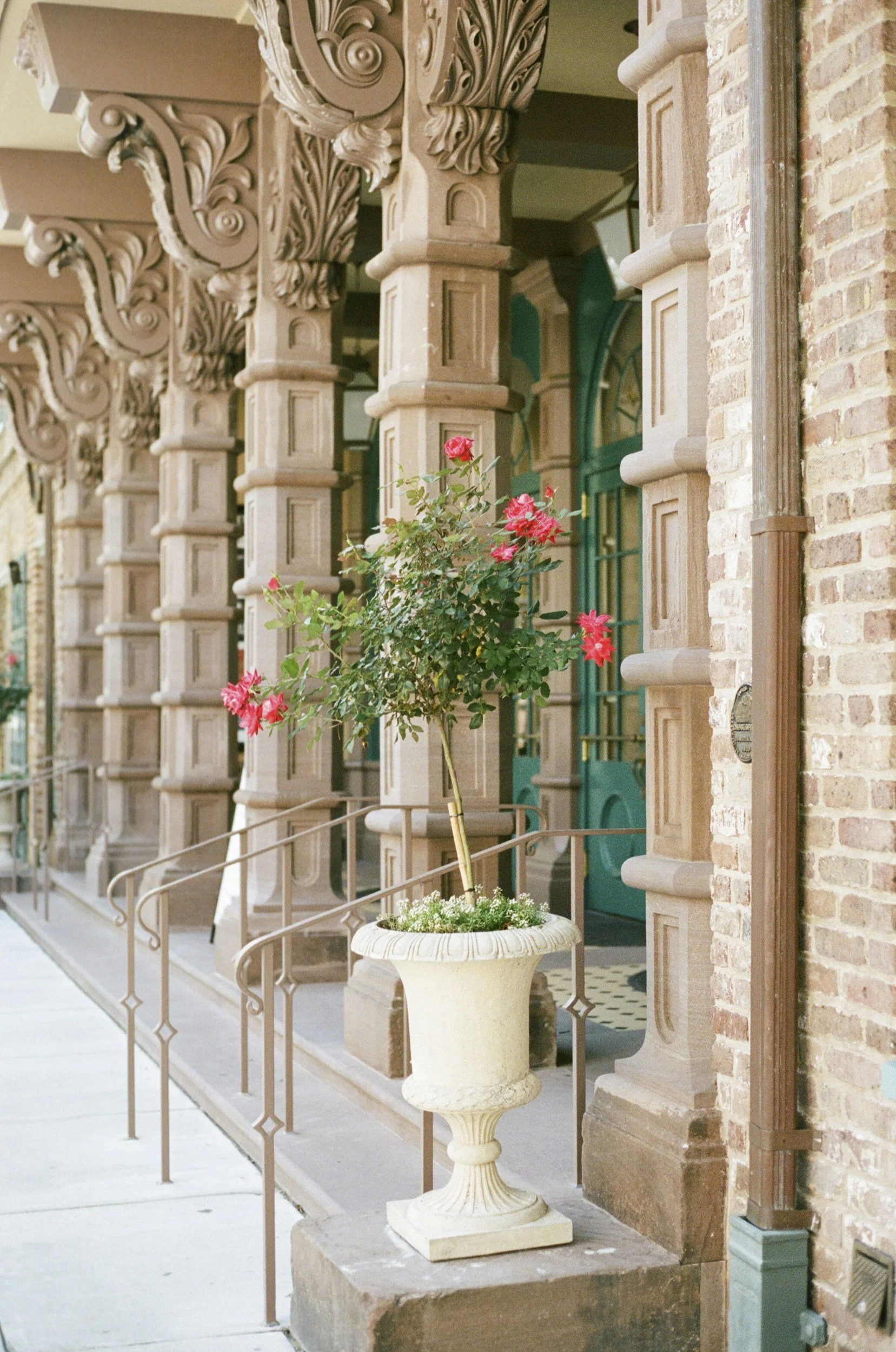 Charleston historic boutique hotel building entrance with ornate columns, brickwork, and a planter of pink flowers