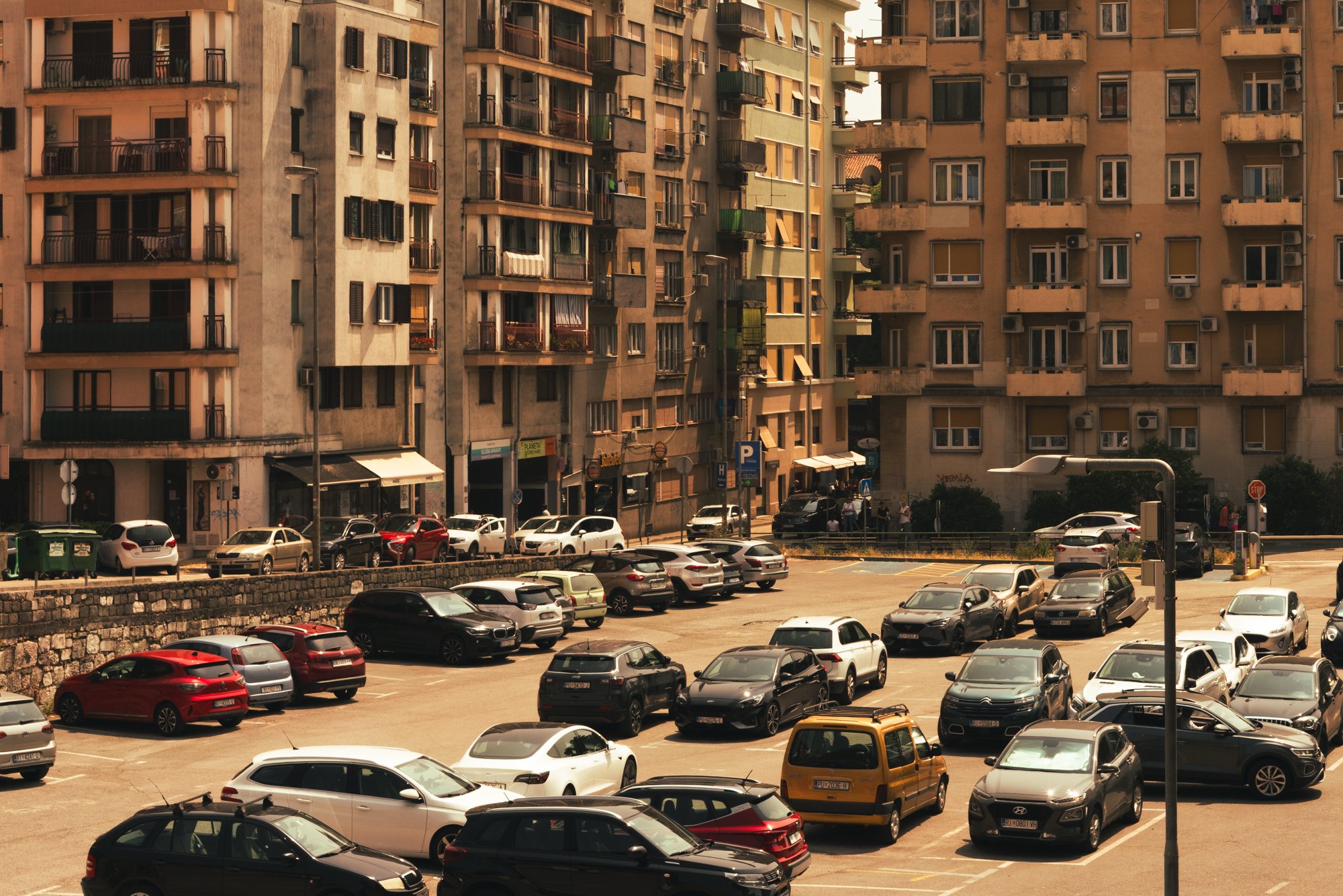 A parking lot filled with various cars in front of tall apartment buildings under sunny weather.