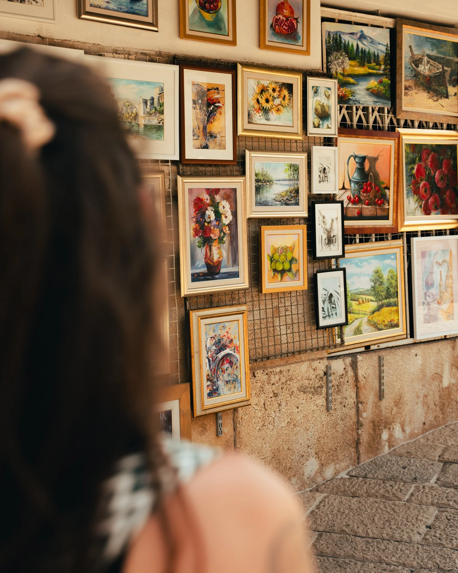 A wall display of various colorful paintings and framed artwork in an art gallery or store.